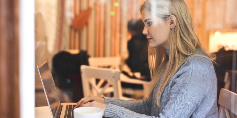 Blonde vrouw achter laptop met koffie op tafel